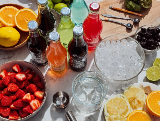 Flat lay of ingredients for pink party punch including soda, cranberry juice, pineapple juice, grenadine, and sliced fruit.