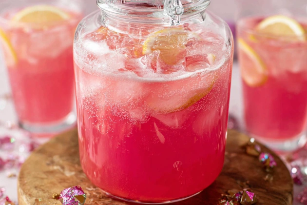 Glasses of pink punch served on a tray with fruit garnishes, festive straws, and pastel napkins.