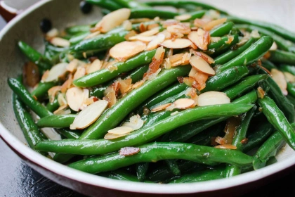 Overhead shot of green beans almondine with golden toasted almonds on a rustic white plate
