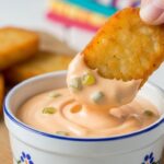 A crispy hash brown being dipped into a small ramekin of creamy homemade Big Mac sauce.