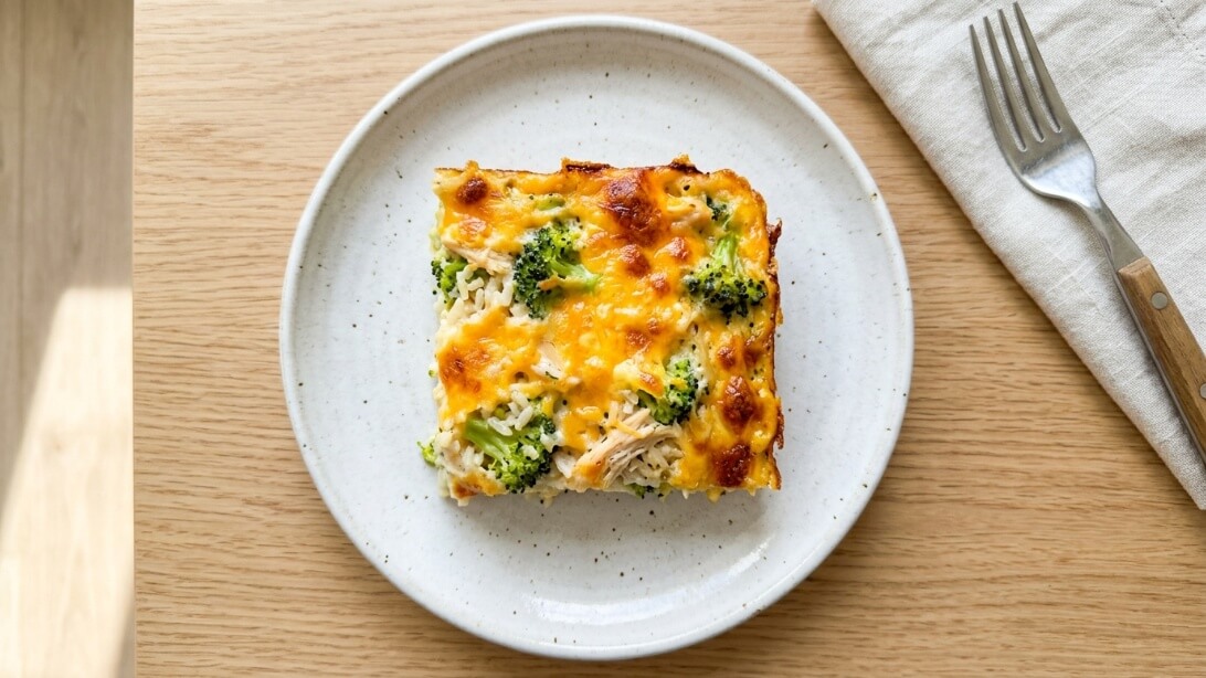 A square slice of cheesy chicken broccoli rice casserole on a white plate